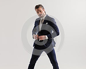 elegant sexy man with glasses posing in a cool way while buttoning high class suit
