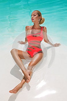 Elegant sexy woman in bikini on the sun-tanned slim and shapely body is posing near the swimming pool. Sunbathing By Swimming Pool