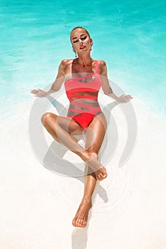 Elegant sexy woman in bikini on the sun-tanned slim and shapely body is posing near the swimming pool. Sunbathing By Swimming Pool