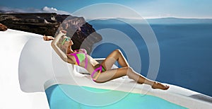Elegant sexy woman in colorful swimsuit is sensually posing on the background of the view of the island of Santorini