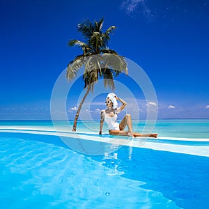 Elegant sexy woman in the white bikini on the sun-tanned slim and shapely body is posing near the swimming pool on Maldives.