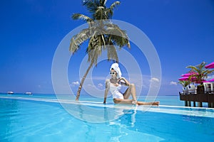 Elegant sexy woman in the white bikini on the sun-tanned slim and shapely body is posing near the swimming pool on Maldives.