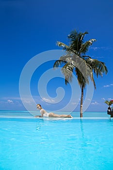 Elegant sexy woman in the white bikini on the sun-tanned slim and shapely body is posing near the swimming pool on Maldives island