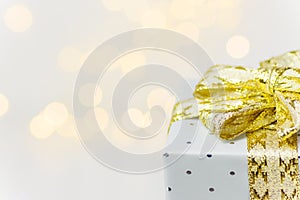 Elegant silver gift box tied with golden ribbon with bow bokeh garland lights on white background. Christmas New Years presents