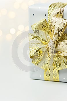 Elegant silver gift box tied with golden ribbon bow bokeh garland lights on white background. Christmas New Years presents holiday
