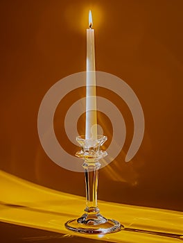 Elegant Single Lit Candle in Crystal Holder on Warm Amber Background with Gentle Drapery