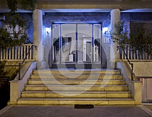 An elegant sixties apartment building`s main entrance, with marble stairs and a framed glass door