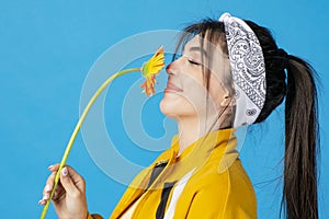 Elegant, slim woman with hair band posing with long orange flower, smelling with closed eyes.