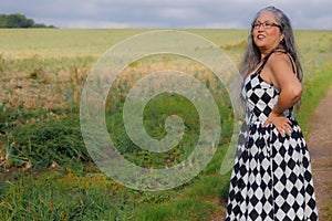 Elegant smiling senior adult woman wearing black and white sundress standing in field