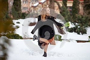 Elegant smiling young woman with long blonde hair in a black coat poses in the city. Portrait of a beautiful modern woman with