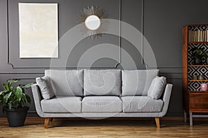 Elegant sofa between a plant a wooden cupboard in a living room interior with a painting and mirror on the wall in a living room