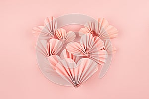 Elegant soft pink paper ribbed heart shape of little hearts in oriental origami style as soar flow on pink background, top view.