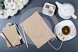Elegant still life - sheet of brown craft paper, notebooks, white chrysanthemums, pencils, teapot, cup of herbal tea