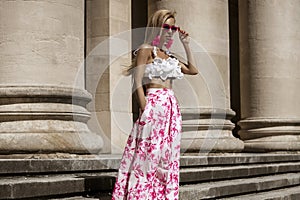 Elegant, stylish woman in pink floral dress and sexy high heels is sensually walking in the city on a sunny summer day. Outdoor