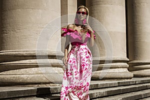 Elegant, stylish woman in pink floral dress and sexy high heels is sensually walking in the city on a sunny summer day. Outdoor