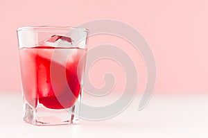 Elegant sweet red strawberry alcoholic cocktail with ice cubes in shot glass in soft light pink bar interior, copy space.