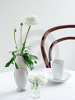Elegant table and a chair setting with white ranunculus flowers and a cup of coffee.