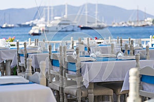 Elegant table setting with fork, knife, wine glass, white plate and blue napkin in restaurant. Turkey. Beach cafe near sea