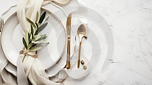 Elegant table setting with white plates, gold cutlery, and olive branch
