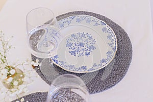 Elegant table setting with wineglass, plate and small glass vase with gypsophila wicker gray table-napkin. Stylish decor