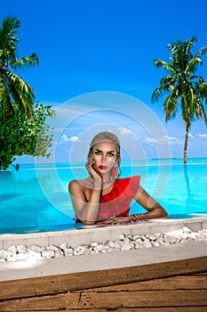 Elegant tanned woman in red swimsuit in pool on tropical Maldives island. Beautiful bikini girl in pool with view on horizon. Sexy