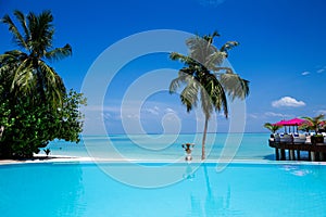 Elegant tanned woman in white swimsuit in pool on tropical Maldives island. Beautiful bikini body girl in pool with view on