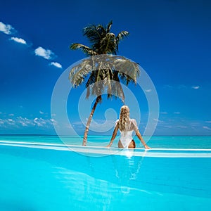 Elegant tanned woman in white swimsuit in pool on tropical Maldives island. Beautiful bikini body girl in pool with view on