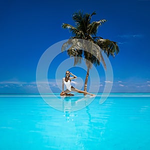 Elegant tanned woman in white swimsuit in pool on tropical Maldives island. Beautiful bikini body girl in pool with view on