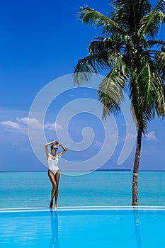 Elegant tanned woman in white swimsuit in pool on tropical Maldives island. Beautiful bikini body girl in pool with view on