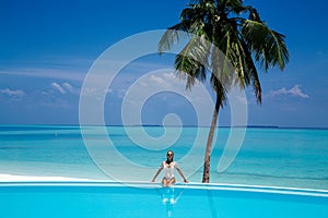 Elegant tanned woman in white swimsuit in pool on tropical Maldives island. Beautiful bikini body girl in pool with view on