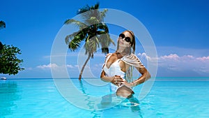 Elegant tanned woman in white swimsuit in pool on tropical Maldives island. Bikini girl in pool with view on horizon. Sexy model