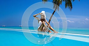 Elegant tanned woman in white swimsuit in pool on tropical Maldives island. Bikini girl in pool with view on horizon. Sexy model