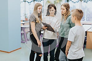 Elegant teacher stands with a black pad and explains something to a group of teenagers during extracurricular activities