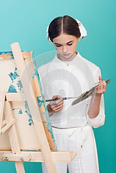 elegant teen artist painting on easel with brush and palette