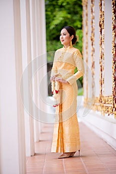 An elegant Thai woman in Thai dress adorned with precious jewelry holds a flower garland in a beautiful ancient Thai temple