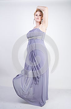 Elegant thick female in a grey long dress. pretty plus size woman in evening dress standing on white studio background. short hair