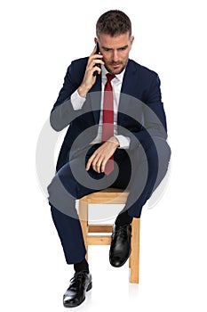 Elegant unshaved businessman with elbow on knee talking on the phone