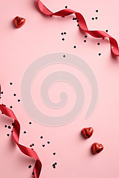 Elegant Valentines Day background with red ribbon, confetti, heart shaped sweets on pink background. Minimal style. Flat lay