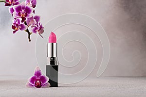 An elegant vibrant pink lipstick beside a beautiful purple orchid flower