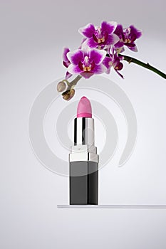 An elegant vibrant pink lipstick beside a beautiful purple orchid flower