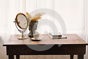 Elegant Vintage Mirror and Bust Vase With Pampas Grass Next to a Coffee Cup on a Wooden Table