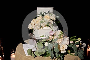 Elegant wedding or birthday cake decorated with fresh rose flowers on table in restaurant, copy space.