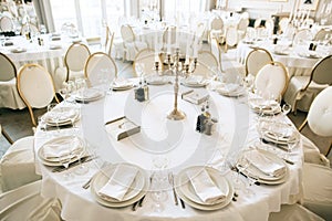 Elegant wedding reception white table arrangement restaurant, candlestick on table. Plates, forks and glasses