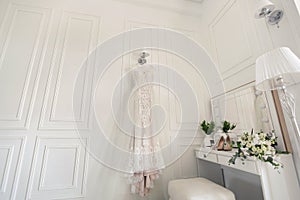 Elegant wedding white dress hanging on a wall during a wedding preparation. Bride's morning. Before ceremony.