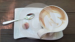 Elegant white cup of cappuccino with tea spoon and small twirl meringue on white stylish plate