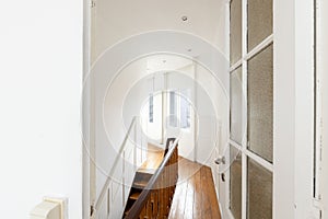Elegant white hallway furnished with a wooden railing and a single armchair