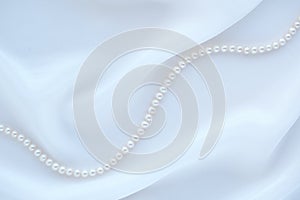 Elegant white silk background with pearl necklace.