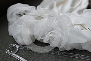 Elegant White Wedding Dress Detail and Clear Plastic Hanger on Grey Background