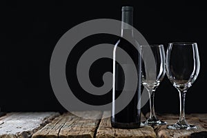 Elegant wine bottle and glasses stands on the rustic wooden table on black background. Space for text. Advertisement concept