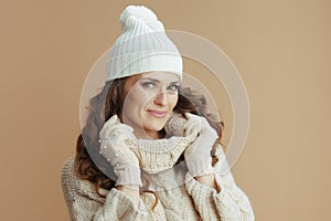 Elegant woman in beige sweater, mittens and hat on beige